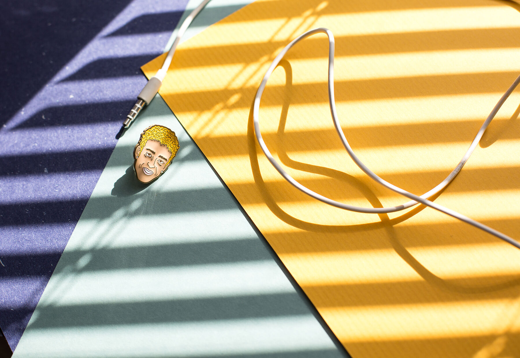 Pin metalowy w lifestyle context — editorial shot na kolorowych pasach z kabelkiem